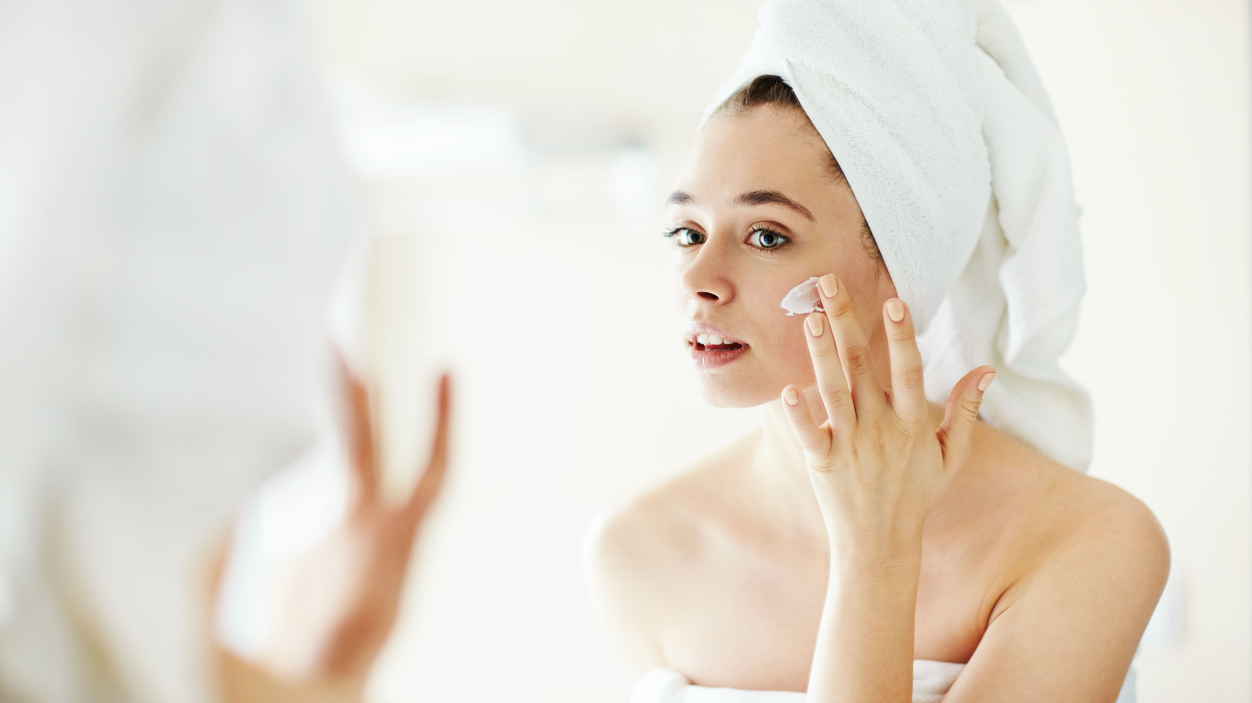 Pretty girl applying moisturizing cream in front of mirror